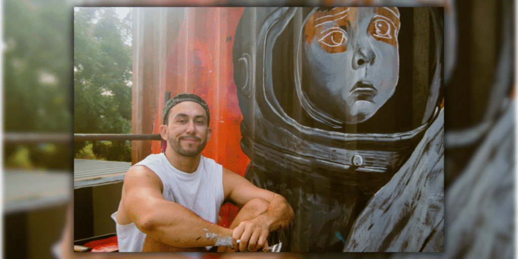 Michel Iniestra, a multidisciplinary artist, poses next to his emotional mural of an astronaut child, reflecting his creative vision.