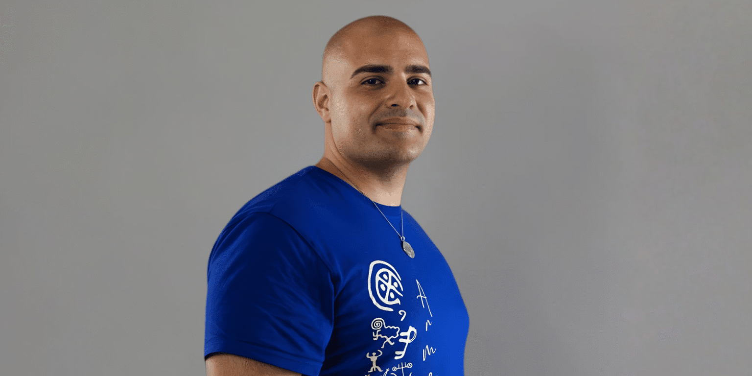 "Arthur Palyan, transformational life coach, smiling confidently in a blue t-shirt featuring the Seven Levels of Self framework design. Arthur’s teachings focus on helping individuals break free from survival mode and embrace conscious living."